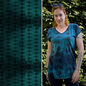 Könnte beinhalten: Ein blaugrünes T-Shirt mit einem dunkelblauen und weißen Muster aus abstrakten Formen. Das Shirt hat einen V-Ausschnitt und kurze Ärmel.