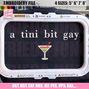 Op de afbeelding: Een borduurontwerp met de tekst "a tini bit gay" en een regenboogcocktailafbeelding. Het ontwerp wordt weergegeven in een borduurring. Beschikbaar in 4 maten: 12,7 cm, 15,2 cm, 17,8 cm en 20,3 cm.