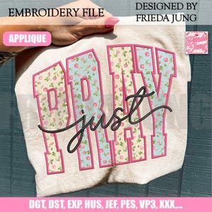 Könnte beinhalten: Eine Stickdatei mit den Worten "PRAY just" in einem floralen Muster, umrandet in Rosa, auf einem hellen Stoff. Das Design enthält den Text "EMBROIDERY FILE" und "DESIGNED BY FRIEDA JUNG". Das Wort "APPLIQUE" ist ebenfalls sichtbar.