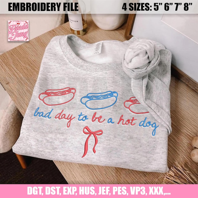 Pu&ograve; includere: Una felpa grigio chiaro con hot dog ricamati rossi e blu e la frase "bad day to be a hot dog". Il design include un fiocco rosso. L'immagine mostra anche "EMBROIDERY FILE" e le opzioni di taglia.