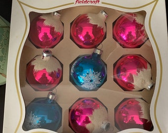 May include: A box of nine vintage glass Christmas ornaments. The ornaments are in a white box with the word "fieldcraft" printed on the top. The ornaments are a mix of pink and blue with white snowflake designs.