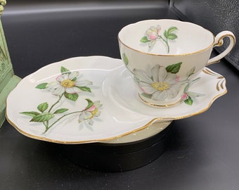 May include: A white porcelain teacup and saucer set with a floral design. The cup and saucer have a gold trim and feature a delicate floral pattern with white flowers and green leaves.
