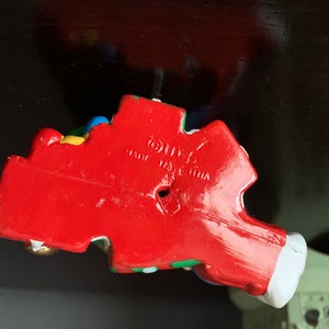 May include: A red, white, blue, green, and yellow plastic figurine of a clown with a red nose and a white hat. The figurine is made in China and has a hole in the bottom.