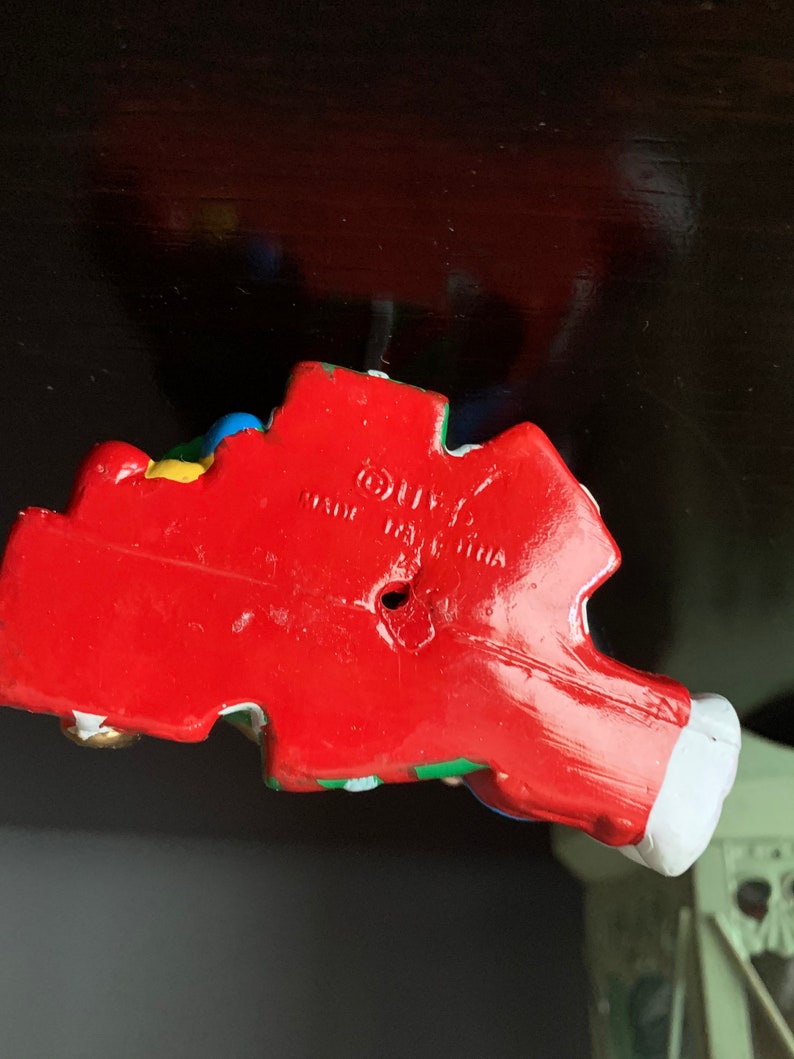 May include: A red, white, blue, green, and yellow plastic figurine of a clown with a red nose and a white hat. The figurine is made in China and has a hole in the bottom.