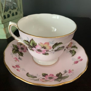 Puede incluir: Un juego de taza y platillo de té rosa con un patrón floral. La taza y el platillo tienen un borde dorado.