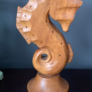 Könnte beinhalten: Eine Holzfigur eines Seepferdchens mit Sockel. Das Seepferdchen hat Löcher, die möglicherweise zum Aufbewahren von Ohrringen oder anderen kleinen Gegenständen dienen.