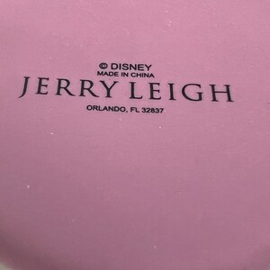 May include: A pink ceramic mug with the text "&copy; DISNEY MADE IN CHINA JERRY LEIGH ORLANDO, FL 32837" printed on the bottom.