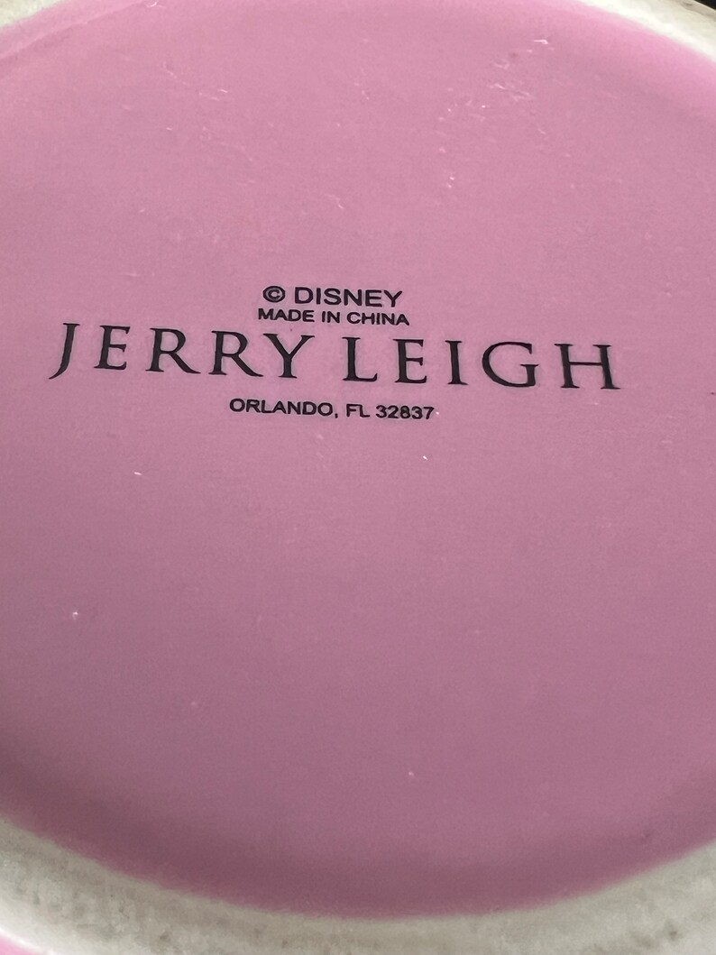 May include: A pink ceramic mug with the text "&copy; DISNEY MADE IN CHINA JERRY LEIGH ORLANDO, FL 32837" printed on the bottom.