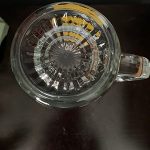 May include: The bottom of a clear glass mug with a textured, ribbed design. The mug has a handle and a yellow rim.