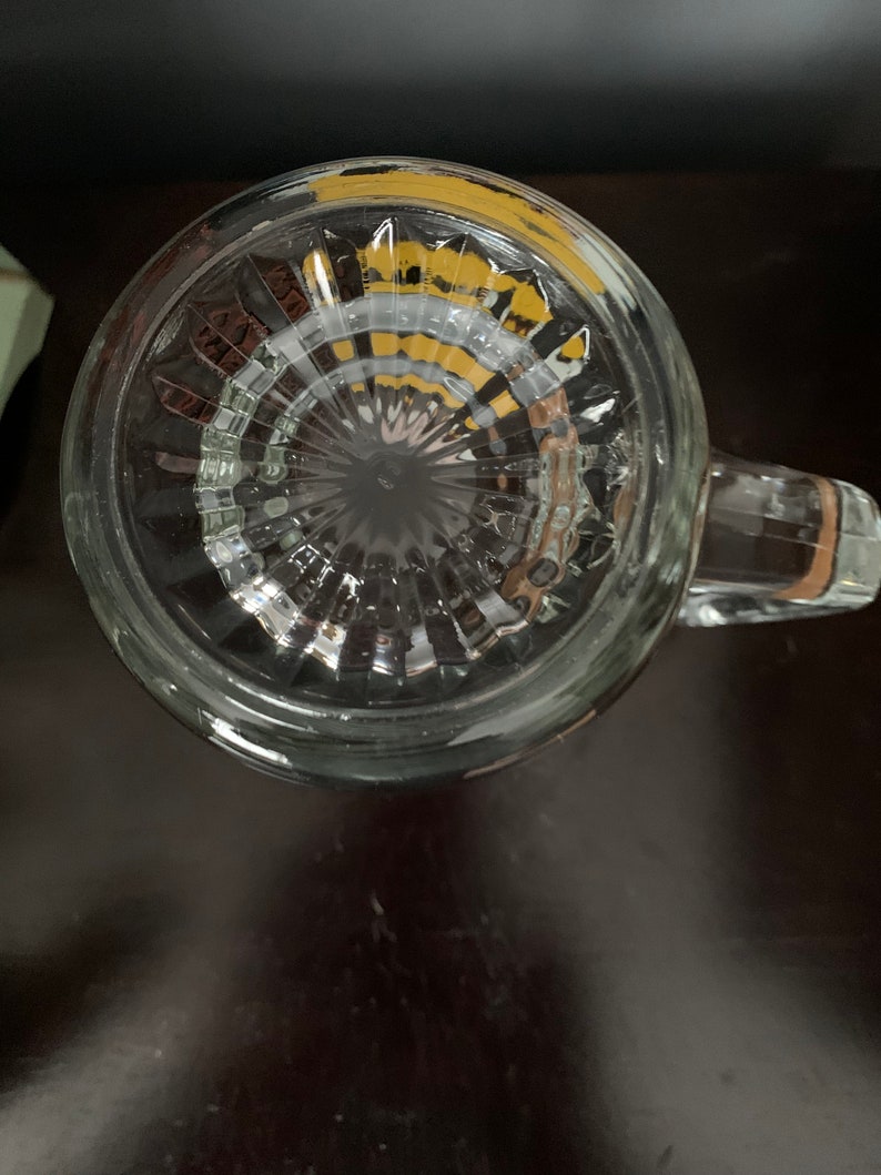 May include: The bottom of a clear glass mug with a textured, ribbed design. The mug has a handle and a yellow rim.