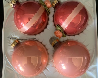 May include: Set of four glass Christmas ornaments in shades of pink and red. Each ornament features a satin ribbon and a small pink rose with green leaves.