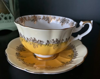 May include: A yellow teacup and saucer with a gold floral pattern. The cup and saucer have a scalloped edge.
