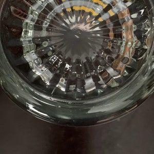 May include: Close-up of the bottom of a clear glass jar with a textured, circular pattern. The jar has a wide rim and a smooth, rounded bottom.