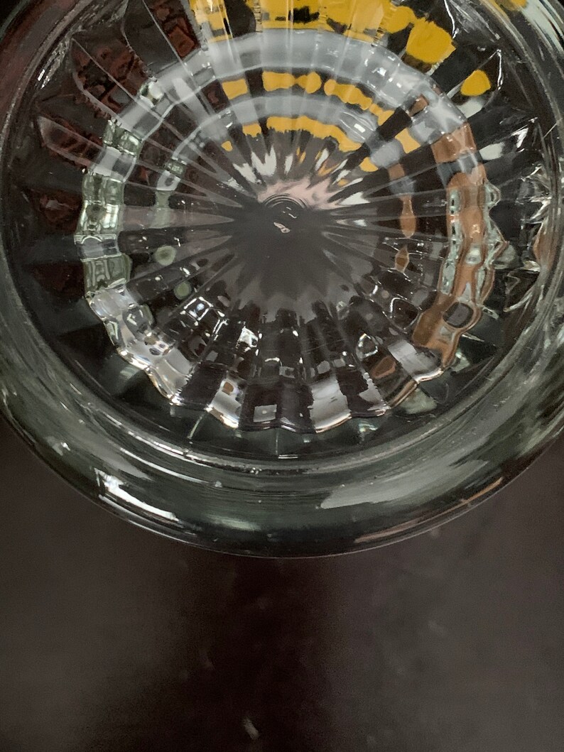 May include: Close-up of the bottom of a clear glass jar with a textured, circular pattern. The jar has a wide rim and a smooth, rounded bottom.
