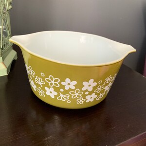 May include: A green ceramic mixing bowl with a white floral pattern. The bowl has a white interior and two handles.