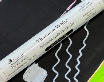 May include: A white Titanium White professional acrylic paint marker with a 3mm round tip, made in England. The marker is shown on a black surface with white paint strokes and a white square. The marker's label includes the brand name and website.