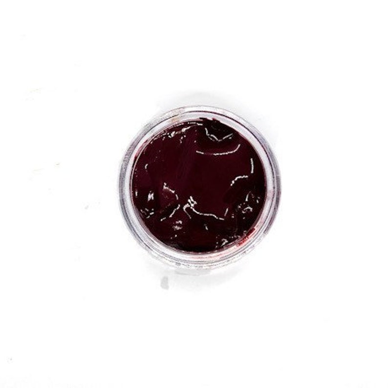 May include: A small, clear jar filled with a dark red, almost black, substance. The substance has a smooth, glossy surface.