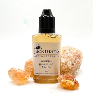 Könnte beinhalten: Eine klare Glasflasche mit schwarzem Verschluss, beschriftet mit "Jackman's Art Materials Kordofan Gum Arabic Solution 30ml www.jackmansartmaterials.co.uk". Die Flasche ist von kleinen, durchsichtigen, bernsteinfarbenen Stücken Gummi Arabicum umgeben.