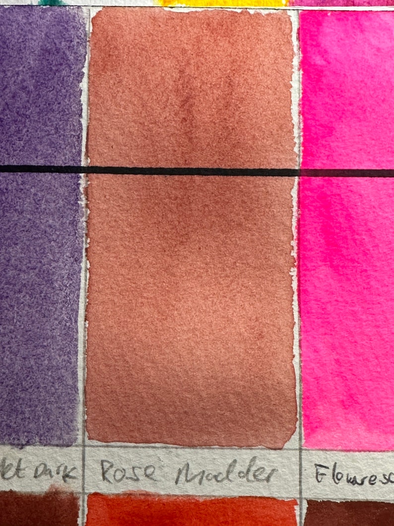 May include: A close-up of a watercolor paint swatch chart. The chart shows three colors: a dark purple, a light brown, and a bright pink. The brown swatch is labeled "Rose Madder".