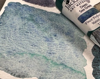 May include: A tube of Jacksons Art Materials Deep Sea Green watercolor paint. The tube is green with a black cap and a white label with the brand name and product information.