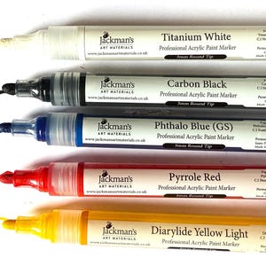 May include: Five acrylic paint markers with a 3mm round tip. The colours are titanium white, carbon black, phthalo blue (GS), pyrrole red, and diarylide yellow light. Each marker has the Jackman's Art Materials logo and website address.