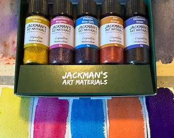 Puede incluir: Un juego de cinco pequeños frascos de vidrio de pinturas de acuarela cristalinas de Jackman's Art Materials. Los colores incluyen amarillo, magenta, azul, naranja y violeta. Cada frasco está etiquetado con el nombre del color y el peso, 6g. La caja es verde.