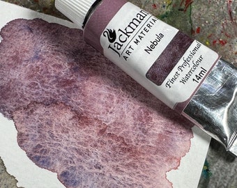 May include: A tube of Jackman Art Materials Nebula watercolor paint, 14ml, next to a watercolor swatch. The paint tube is purple with white text and a swan logo. The swatch shows a blend of purple and red hues.
