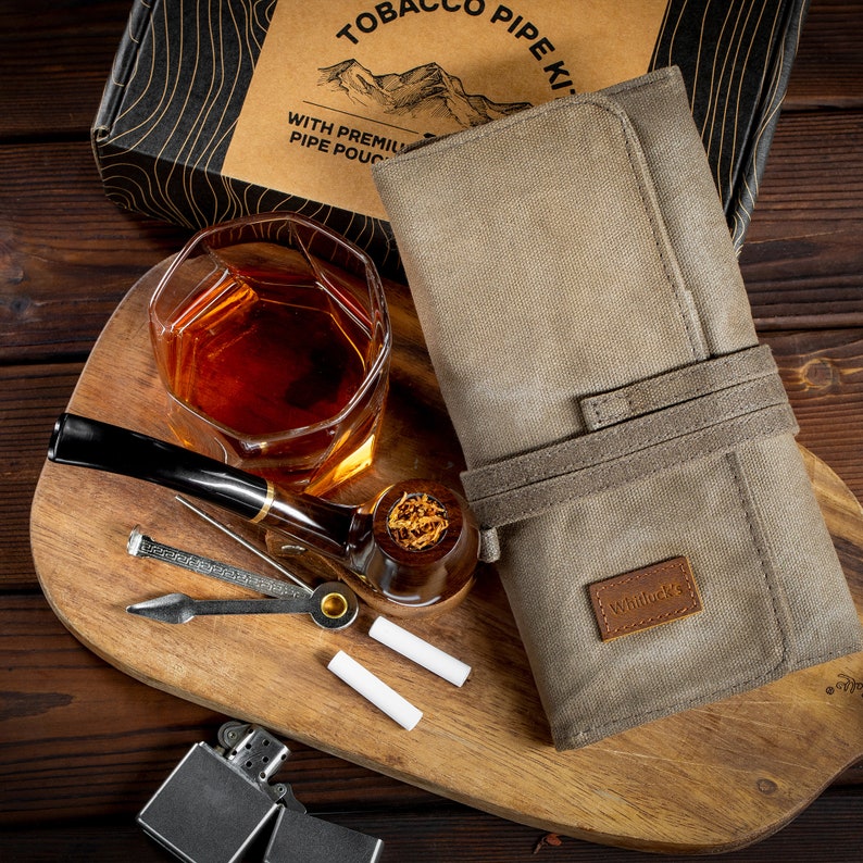 May include: A tobacco pipe kit with a brown leather pouch, a wooden pipe, a glass of whiskey, a lighter, and a pipe tamper. The pouch has the text "Tobacco Pipe Kit" and "With Premium Pipe Pouch" printed on it. The pouch also has the brand name "Whitluck's" printed on it.