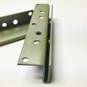 May include: Two olive-green metal brackets with multiple circular holes. The brackets are L-shaped and appear to be new. The image is taken on a white background. The brackets are likely for shelving or construction.