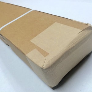 May include: A brown cardboard box with tape sealing the edges. The box is wrapped in brown paper and has a white string tied around it.