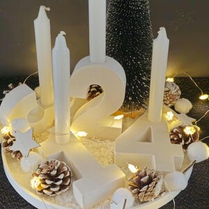 K&ouml;nnte beinhalten: Wei&szlig;er Holz-Adventskalender mit vier Kerzen, einem kleinen Tannenbaum und wei&szlig;en Lichtern. Die Zahlen 1, 2, 3 und 4 sind auf dem Kalender abgebildet.