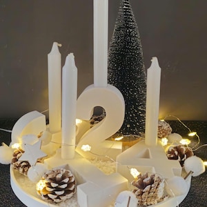 Adventskranz ganz in weiß, mit weißen Buchstaben von 1-4 auf einem weissen Tablett, alles wurde aus  hochwertigem Gießbetonpulver hergestellt.Geschmückt wird es von einem Kunstschnee, einem Tannenbaum und einer Lichterkette mit Sternen und Zapfen