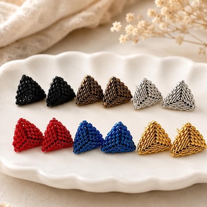 Puede incluir: Una colección de seis pares de pendientes triangulares hechos de pequeñas cuentas uniformes. Los pendientes están dispuestos en dos filas y presentan una variedad de colores que incluyen tonos negro, bronce, plata, rojo, azul y dorado metálico.