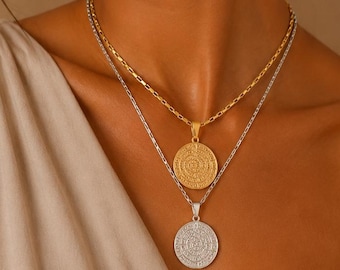 Peut inclure: Un ensemble de colliers superposés composé de deux chaînes distinctes. La chaîne la plus courte est dorée avec un design à maillons rectangulaires texturés et un pendentif pièce ronde. La chaîne plus longue est argentée avec un pendentif pièce ronde.