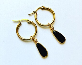 May include: A pair of gold hoop earrings with black teardrop-shaped charms. The earrings are simple and elegant.
