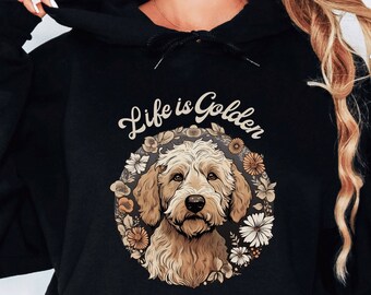 以下が含まれることがあります： 花に囲まれたゴールデン・ドゥードル犬と「Life is Golden」の文字がプリントされた黒いパーカー。
