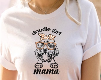 Puede incluir: Camiseta blanca con un gráfico de doodle girl mama. El gráfico presenta un perro doodle con gafas y una diadema de lunares.
