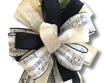 May include: A large bow made with black, cream, and white ribbon with a musical note pattern. The bow is tied with a knot in the center.