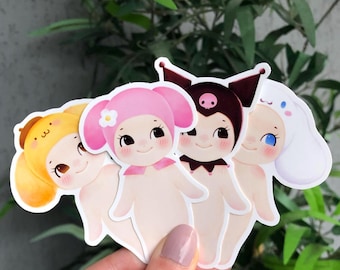 May include: A selection of four die-cut stickers showcasing cartoon characters. The stickers feature figures in yellow, pink, and brown, each with unique hats and facial expressions. The stickers are held against a backdrop of green leaves.
