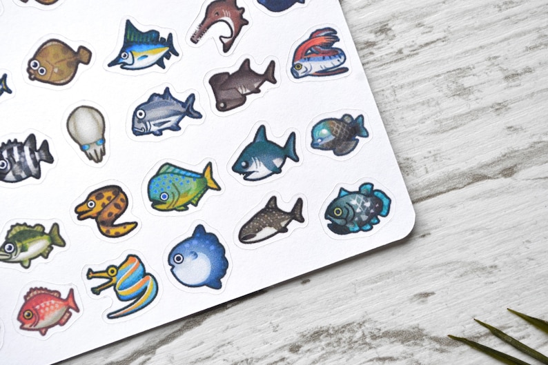 May include: A sheet of colourful stickers featuring various types of fish, including a shark, a pufferfish, a moray eel, and a swordfish. The stickers are on a white background.