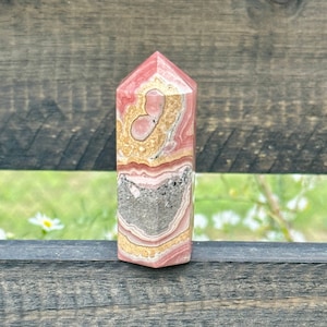 May include: A pink, brown, and gray banded crystal point. The crystal is polished and has a pointed tip.