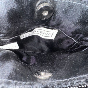 May include: Inside view of a black purse with a silver snap closure and a black label that reads "Regale".