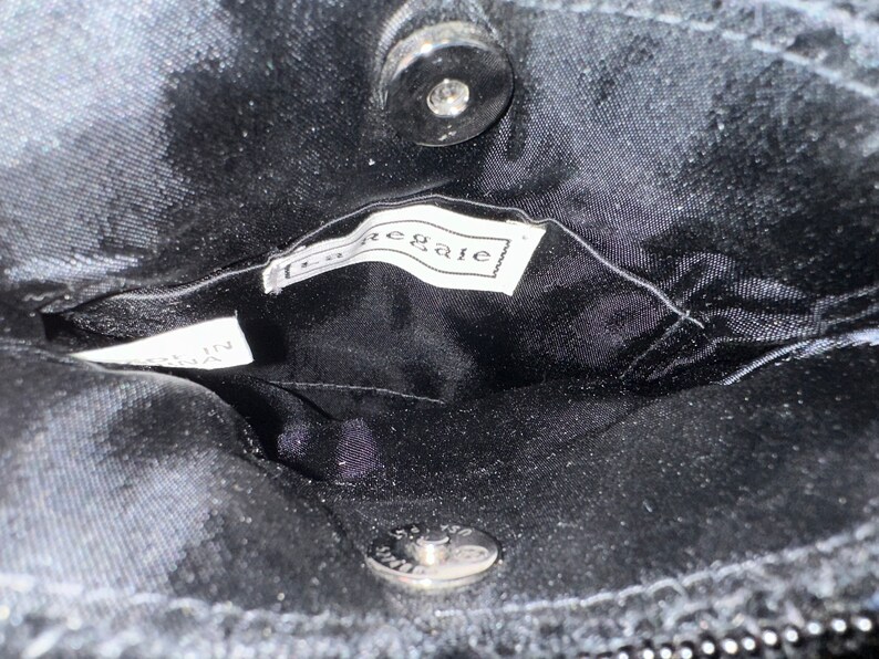 May include: Inside view of a black purse with a silver snap closure and a black label that reads "Regale".