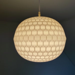 Op de afbeelding: Een witte, ronde, hangende lamp met een getextureerd, honingraatpatroon.