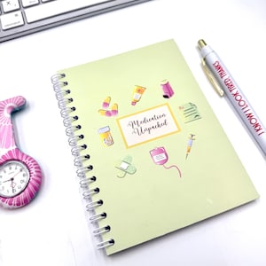 May include: A pale green spiral-bound notebook featuring the words "Medication Unpacked" and medical illustrations. A pen with the text "I KNOW I LOOK TIRED, THANKS" and a pink nurse's fob watch are also visible.