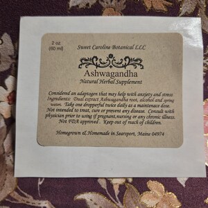 Puede incluir: Una etiqueta rectangular con el texto "Ashwagandha Natural Herbal Supplement". La etiqueta tambi&eacute;n incluye el texto "2 oz (60 ml)" y otros detalles del producto.