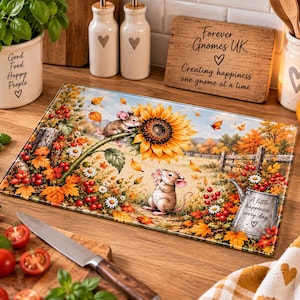 Puede incluir: Una tabla de cortar rectangular de cristal con una escena otoñal que muestra dos ratones, un girasol grande, hojas caídas, bayas rojas y una regadera de metal con el texto A little happiness every day y un corazón impresos.