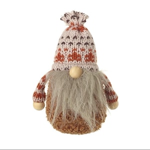 May include: A decorative gnome figure with a knitted hat and arms. The hat has a pattern of brown and orange diamonds on a light grey background. The gnome has a long grey beard and a brown body.