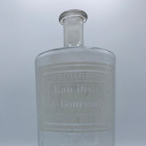May include: A clear glass bottle with a white label that reads "Eau Dist: de Bourrach".