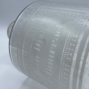 May include: A clear glass bottle with an etched design. The bottle is labeled "Paul Dis. de Bourjac".